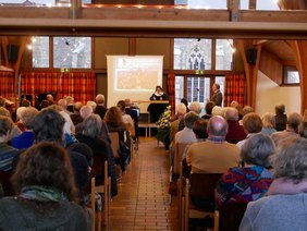 Das Foto zeigt den vollbesetzten Gemeindesaal in Engelskirchen mit der Referentin vorn am Pult. Sie trägt Ordenstracht 