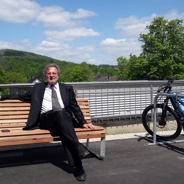 Das Foto zeigt Pfarrer i.R. Thomas Werner auf der neuen Bank vorm Kreiskirchenamt 