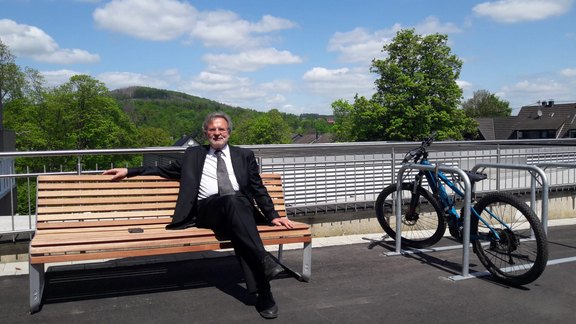 Das Foto zeigt Pfarrer i.R. Thomas Werner auf der neuen Bank vorm Kreiskirchenamt 