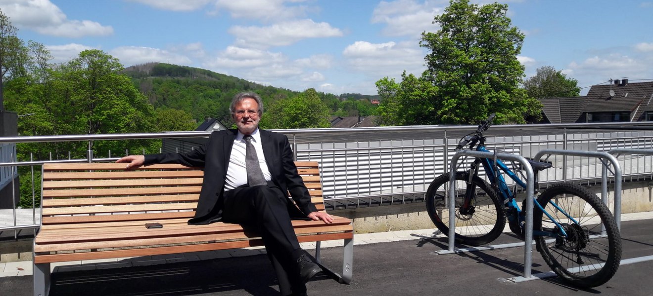 Das Foto zeigt Pfarrer i.R. Thomas Werner auf der neuen Bank vorm Kreiskirchenamt 