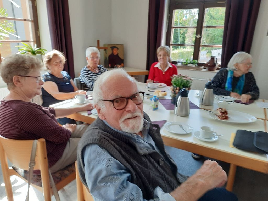 Das Bild zeigt ein Treffen der Trauergruppe. Ein älterer Herr dreht sich zum Betrachter um   