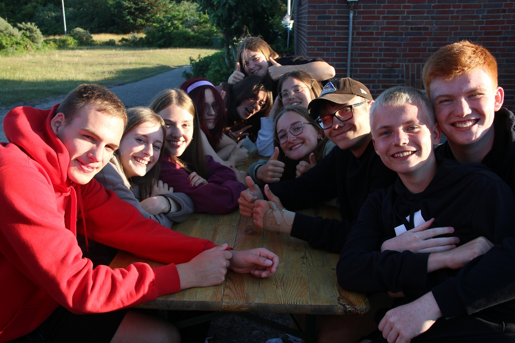 Das Foto zeigt lachende Jugendliche an einem Tisch draußen sitzend